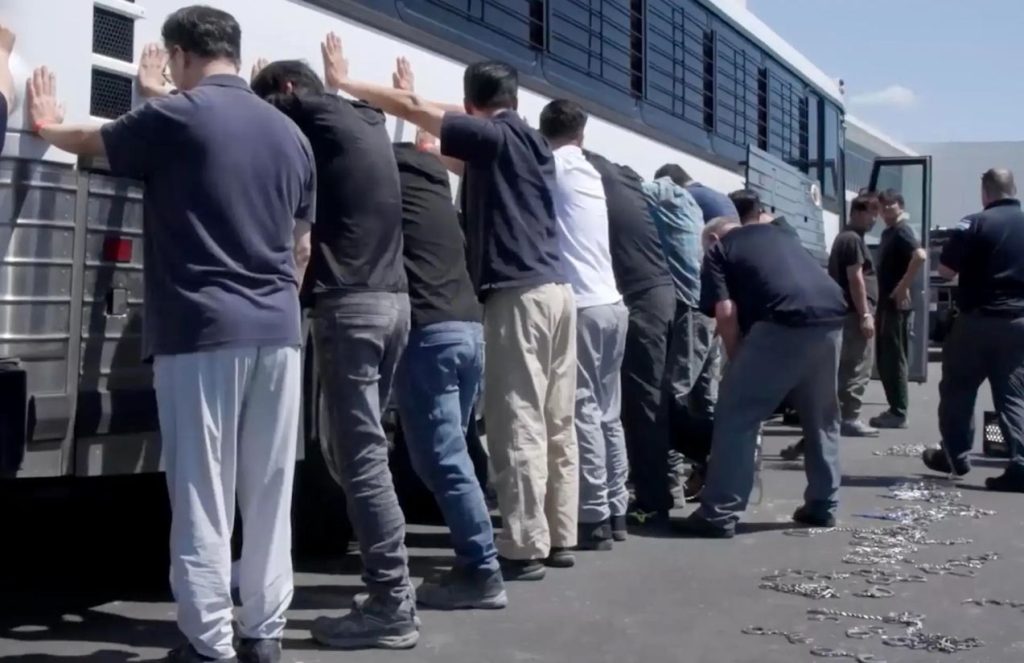 Several people being detained, lined up against a wall for a search