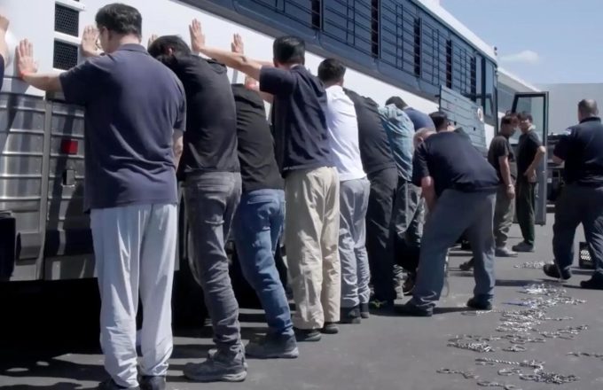 Several people being detained, lined up against a wall for a search
