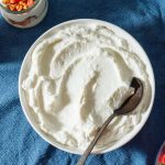 A large bowl filled with white Greek yogurt, with small jars of strawberries beside it