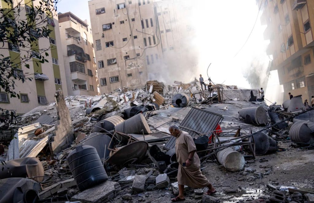 Several people walking over a building destroyed by an Israeli attack