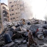 Several people walking over a building destroyed by an Israeli attack