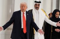 Donald Trump and the leader of Qatar walking down a hallway while raising their arms as if complaining about something
