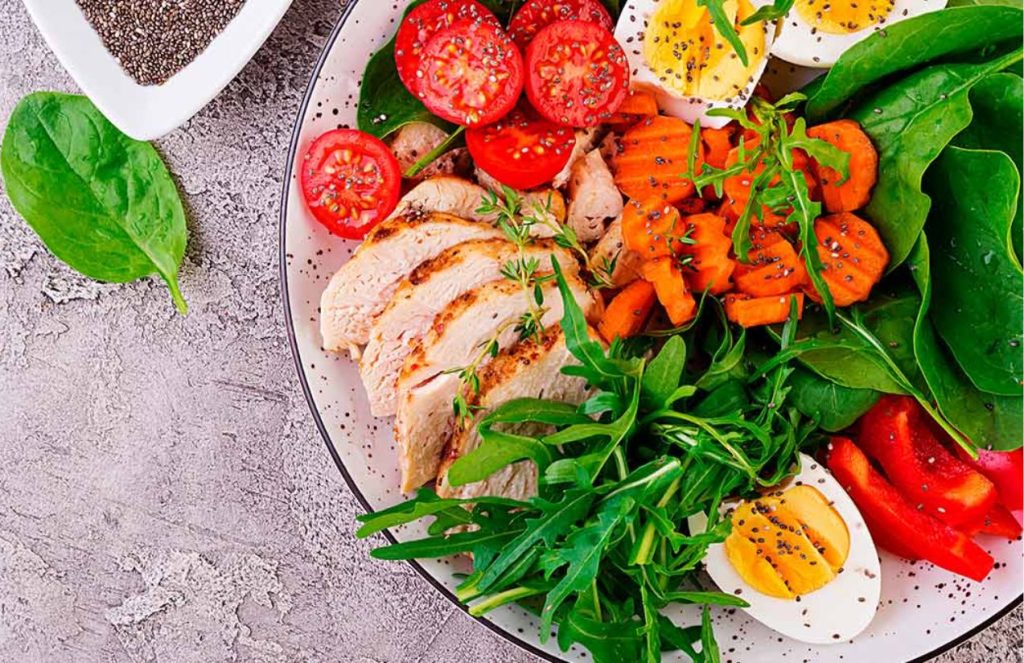 A delicious plate of salad with green and colorful vegetables accompanied by a piece of chicken