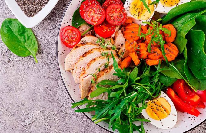 A delicious plate of salad with green and colorful vegetables accompanied by a piece of chicken