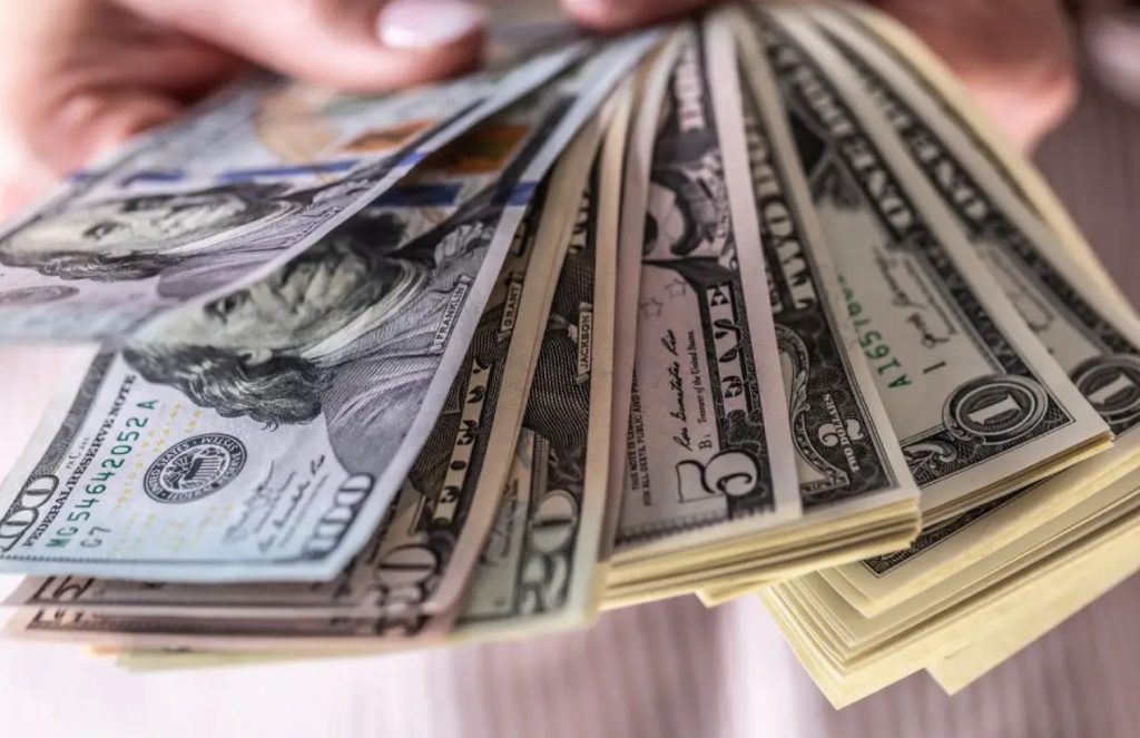 A person holding and counting a stack of $1, $5, $20, $50, and $100 bills