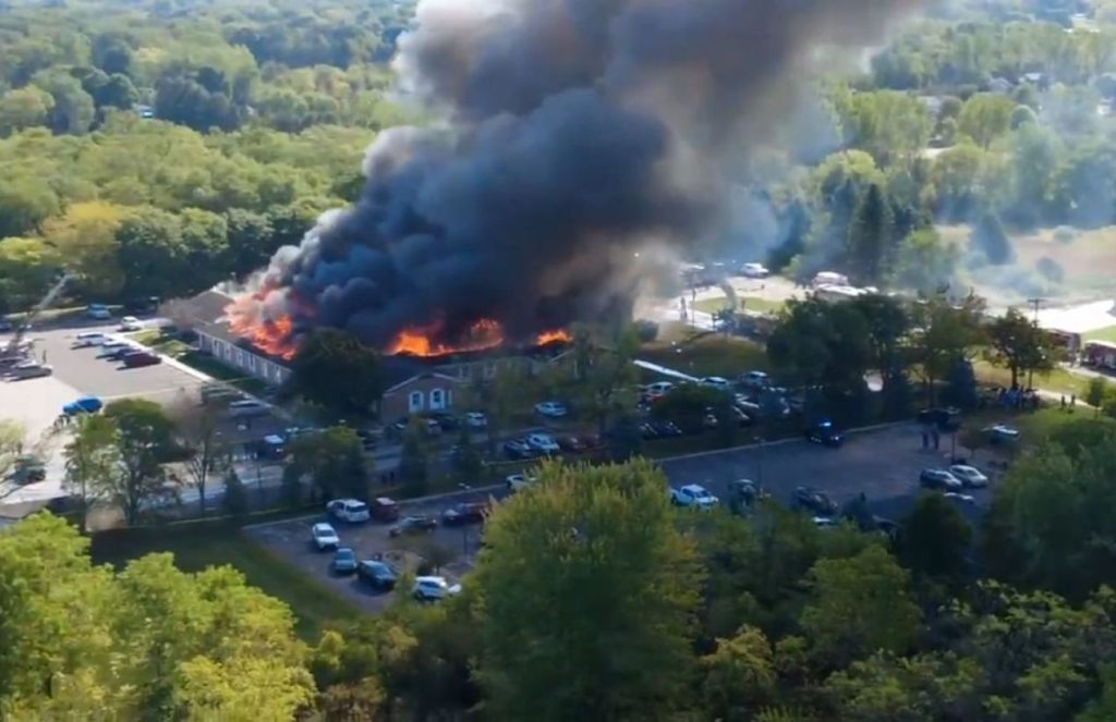 A church engulfed in flames with many police cars around it watching the scene