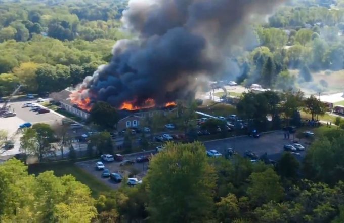 A church engulfed in flames with many police cars around it watching the scene