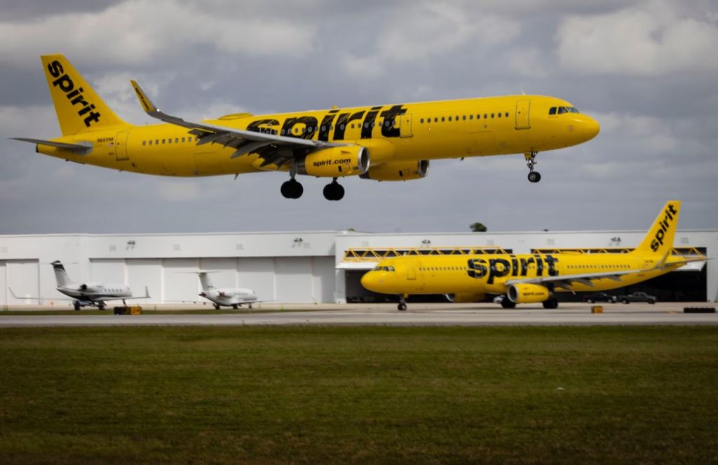 Two Spirit Airlines planes in their striking yellow color, one parked and the other flying above it