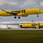 Two Spirit Airlines planes in their striking yellow color, one parked and the other flying above it
