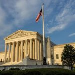 The building of the United States Supreme Court in its striking and imposing white color, with a flag of the same country at its entrance