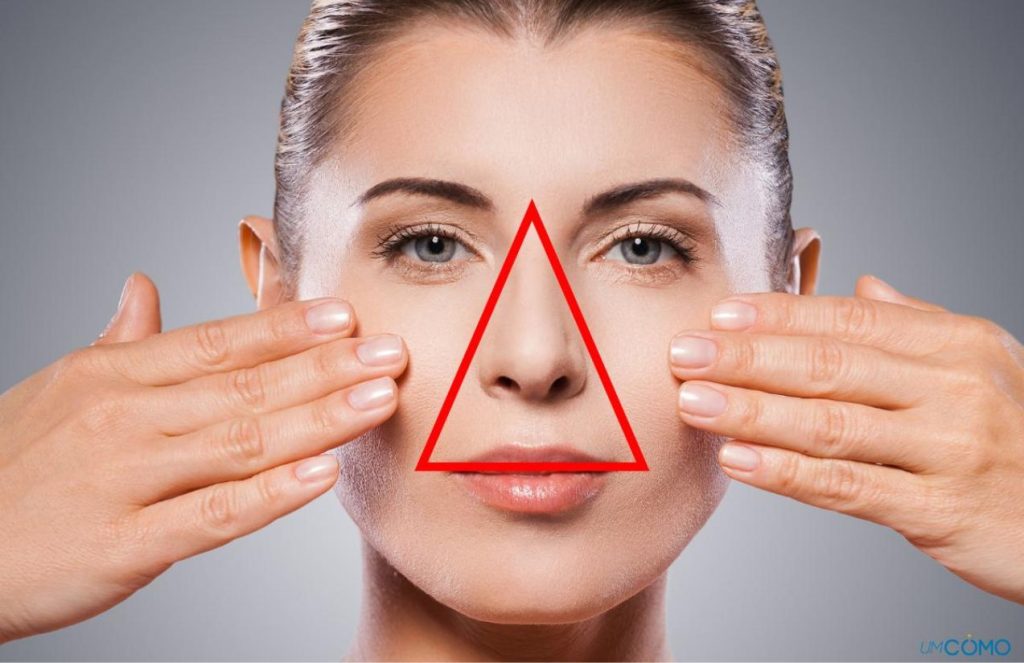 A woman pointing to her face with both hands, with a red triangle marked in the same area