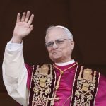 The current Pope appearing in the papal office, wearing his traditional red attire and greeting everyone with his right hand