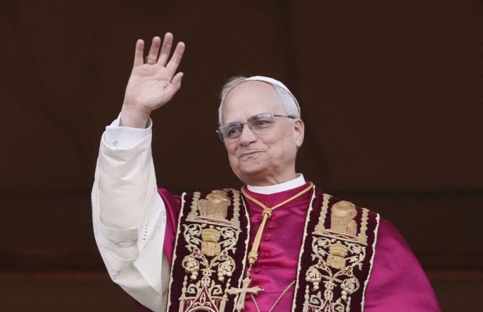 The current Pope appearing in the papal office, wearing his traditional red attire and greeting everyone with his right hand