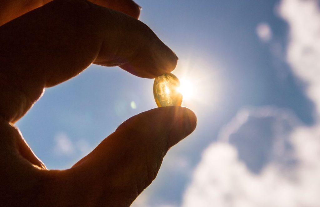 A hand holding a vitamin D pill next to sunlight