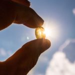 A hand holding a vitamin D pill next to sunlight