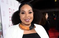 The well-known TV actress posing on the red carpet, wearing a black blouse with a white jacket over it