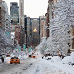 One of the streets of New York covered in snow, with a few people walking and some cars passing by