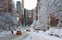 One of the streets of New York covered in snow, with a few people walking and some cars passing by