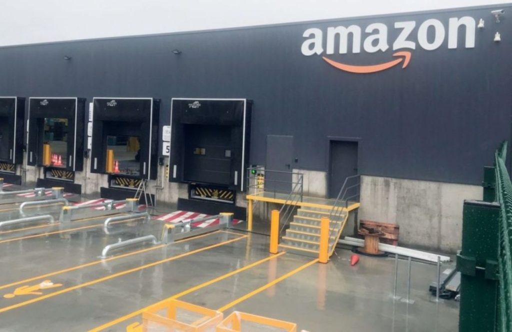 Amazon announces layoffs of 14,000 corporate employees amid the AI era An Amazon warehouse painted black with multiple loading bays for truck dispatch
