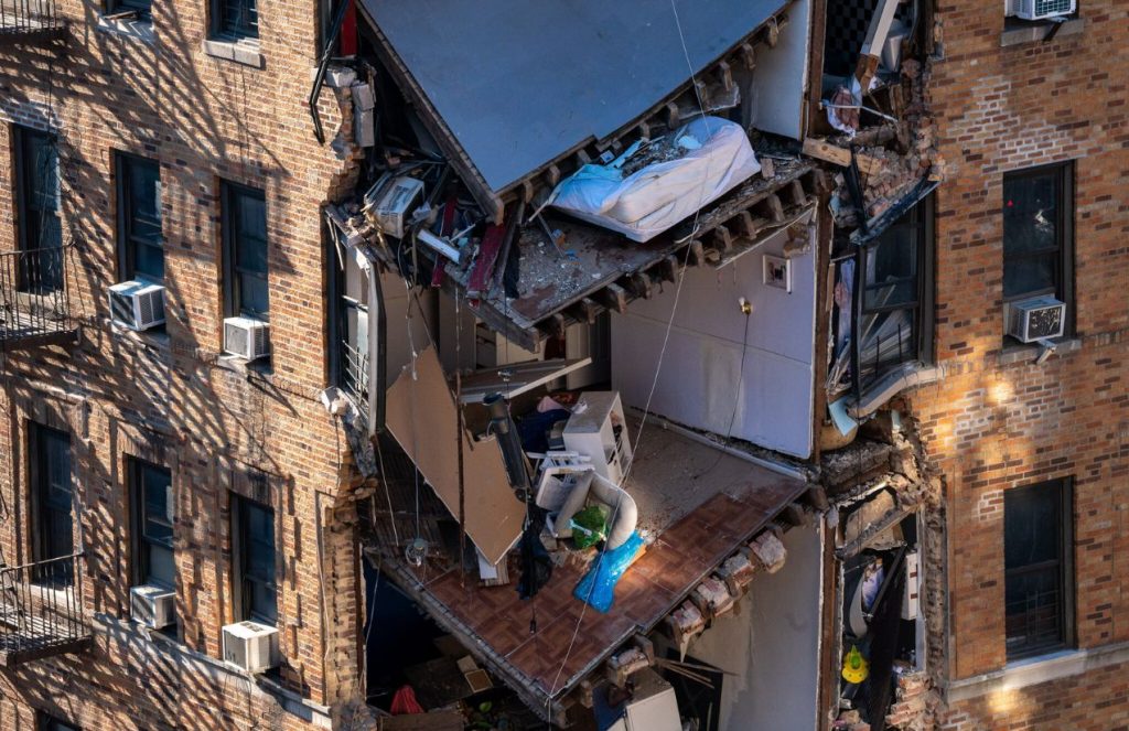 A brick building with part of it collapsed, where some families’ belongings can be seen hanging from the rubble