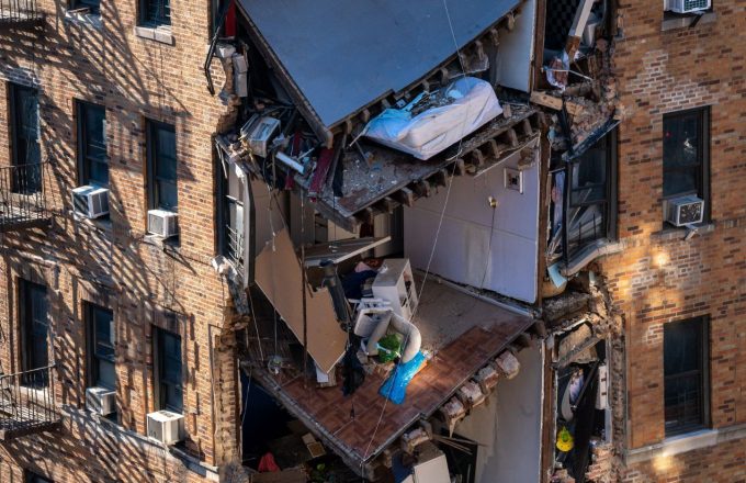A brick building with part of it collapsed, where some families’ belongings can be seen hanging from the rubble