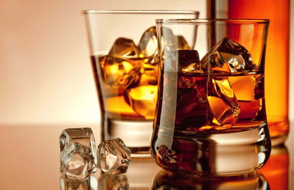 Two glasses filled with liquor and ice on a table