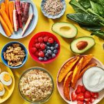 A yellow table filled with healthy foods, including nuts, berries, vegetables, and other nutritious items