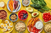 A yellow table filled with healthy foods, including nuts, berries, vegetables, and other nutritious items