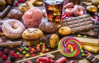 A large wooden table filled with sugary products such as Coca-Cola bottles, donuts, candies, puddings, and other sweets