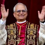 The current pope appearing on the Vatican balcony wearing red robes and raising his arms to greet the crowd
