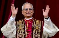 The current pope appearing on the Vatican balcony wearing red robes and raising his arms to greet the crowd