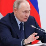 Putin sitting at a table, speaking into a microphone alongside his political associates