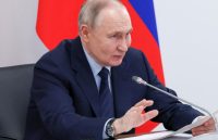 Putin sitting at a table, speaking into a microphone alongside his political associates