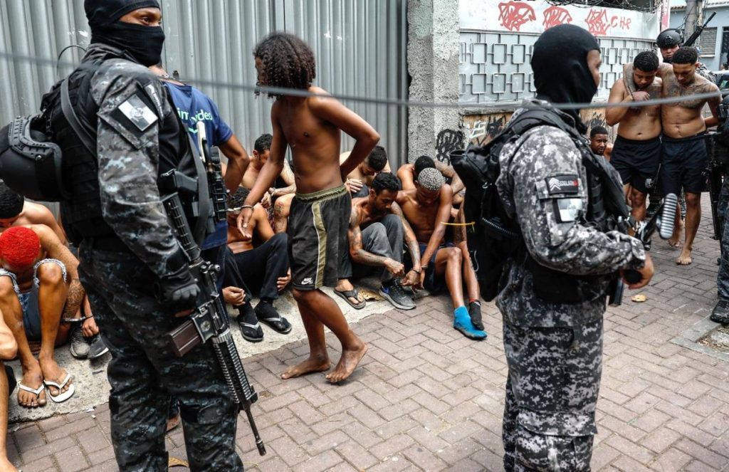 Armed men detaining several shirtless individuals believed to be members of favela gangs in Brazil