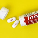 A bottle of Tylenol pills lying on a yellow background with two pills from its contents outside