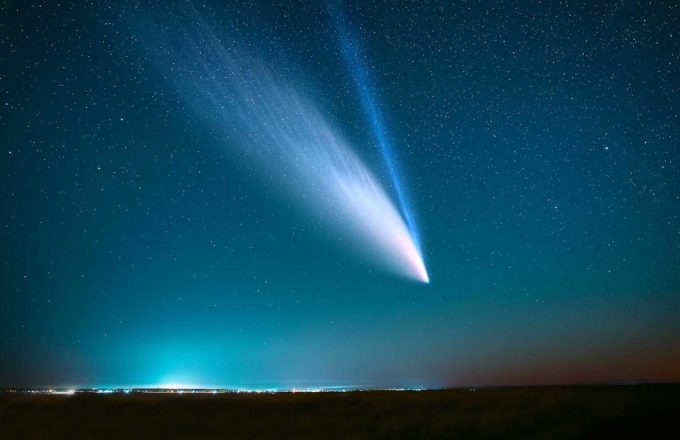 A comet leaving its glowing trail across the night sky above a city