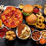 Many ultra-processed foods on a table, including pizzas, hamburgers, onion rings, donuts, and more