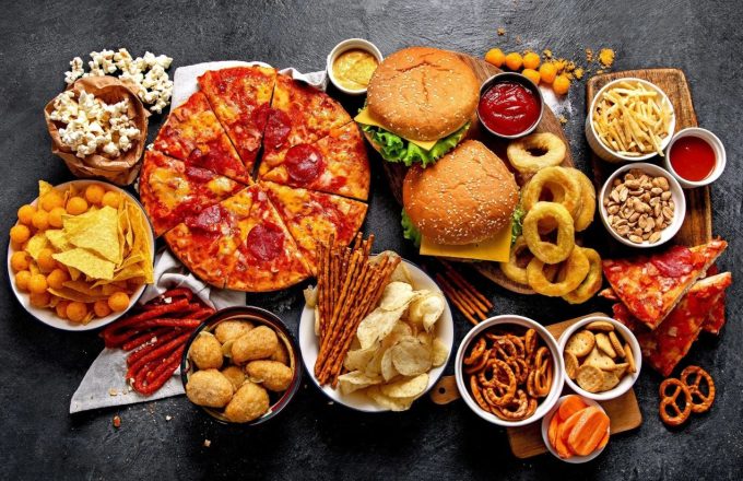 Many ultra-processed foods on a table, including pizzas, hamburgers, onion rings, donuts, and more