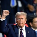 Donald Trump raising his right hand with a clenched fist during an interview, symbolizing strength and determination