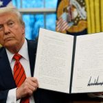 Trump holding up with both hands the signed document on this year’s new tariffs