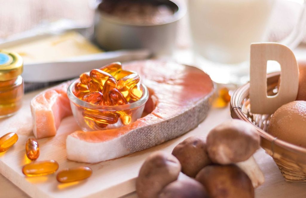 Several vitamin-D-rich foods placed on a table, fish, eggs, mushrooms, along with a cup filled with natural vitamin supplements