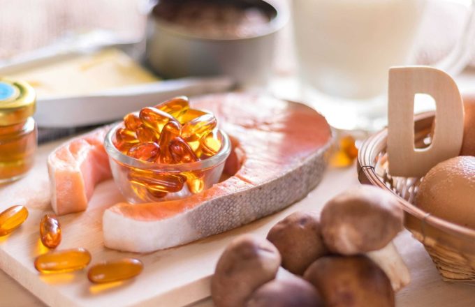 Several vitamin-D-rich foods placed on a table, fish, eggs, mushrooms, along with a cup filled with natural vitamin supplements