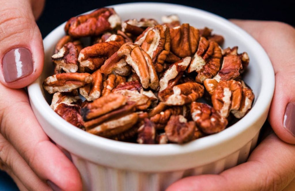 A person’s hands holding a bowl of pecan nuts that look delicious