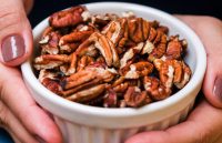 A person’s hands holding a bowl of pecan nuts that look delicious
