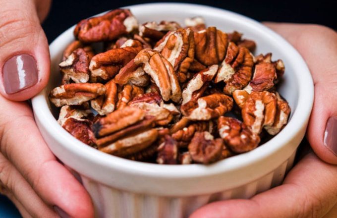 A person’s hands holding a bowl of pecan nuts that look delicious