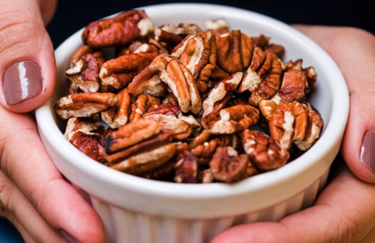 A person’s hands holding a bowl of pecan nuts that look delicious