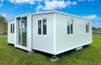 A white Amazon prefab house placed on top of several stones to elevate it off the ground