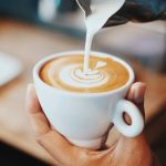 The hands of a barista preparing a cup of coffee with a heart-shaped design