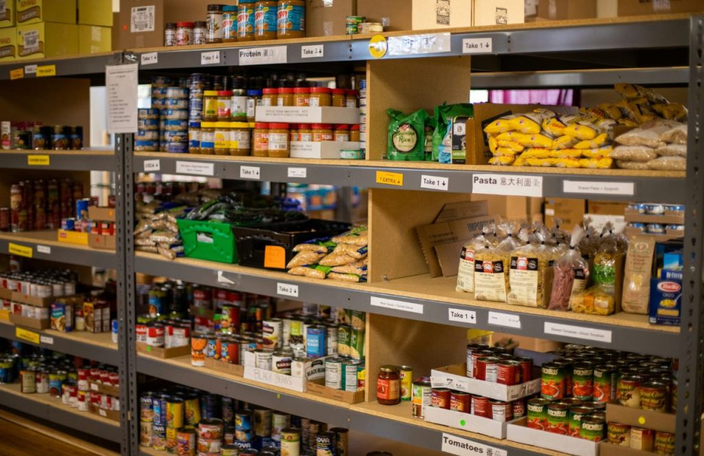A food bank shelf filled with all kinds of canned goods and fresh fruits
