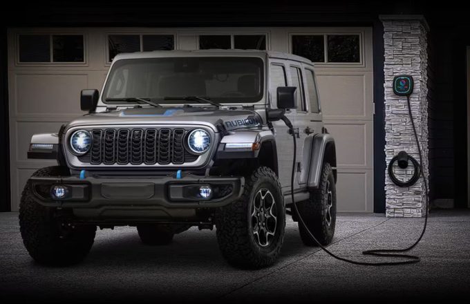 One of the new black electric Jeeps connected to its charger with the front headlights on